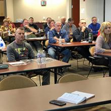 FirstNet Authority Senior Public Safety Advisor Kristi Wilde speaks in front of a group of emergency communications professionals seated behind desks 