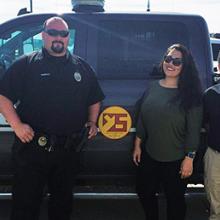 Two men and one woman stand in front of a Yankton Police truck. One of the men wears a police uniform.