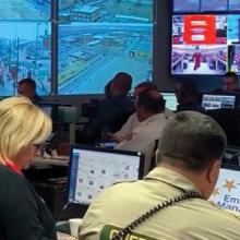 Emergency managers monitor computers during Kansas City Chiefs Super Bowl Parade; large screen projects live camera streams in emergency operations center in Kansas City, Missouri. 