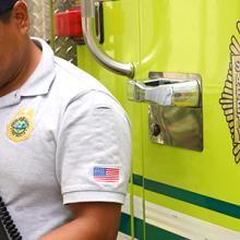 Fire fighter standing in front of a fire apparatus wearing a radio while typing on a mobile device. Fire fighter standing in front of a fire apparatus wearing a radio while typing on a mobile device.