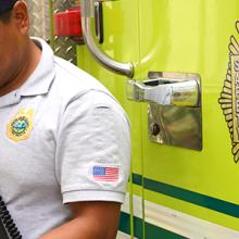 Fire fighter standing in front of a fire apparatus wearing a radio while typing on a mobile device.