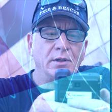 Three police officers consult information on a smartphone, a firefighter looks at a rugged device, an EMS technician next to a patient gurney in the back of an ambulance looks down at a smart device