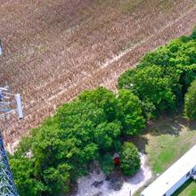 Aerial view of the top of a FirstNet cell site tower with a field and grove of trees in the background.