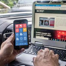 A police officer uses a FirstNet phone and a mobile computing device in his vhicle 