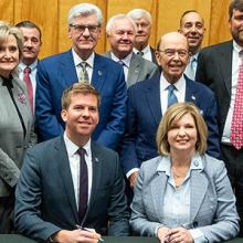 Edward Parkinson of the FirstNet Authority and LouAnn Woodward of UMMC sit in front of the Memorandum of Understanding they have just signed, behind them are standing over a dozen representatives from their organizations Edward Parkinson of the FirstNet Authority and LouAnn Woodward of UMMC sit in front of the Memorandum of Understanding they have just signed, behind them are standing over a dozen representatives from their organizations