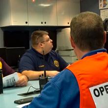 Emergency management and public safety professionals sit around a conference table in discussion.