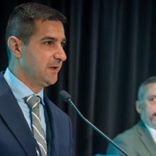 Chief Peter Burke of the Hyannis Fire Department in Massachusetts stands behind podium giving acceptance speech for the inaugural FirstNet Authority Patriot Award; FirstNet Authority Chief Market Engagement Officer Jeremy Zollo and Executive Director / CEO Joe Wassel look on