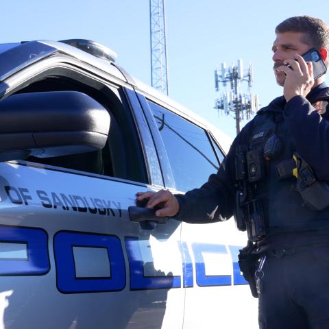 A Sandusky police officer speaks on a FirstNet phone near his patrol vehicle