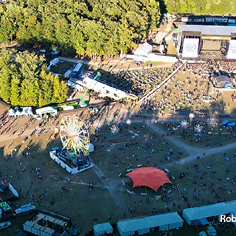 An aerial view of the Firefly Musical Festival grounds, crowds of people at several live music stages around the grounds, a packed parking lot
