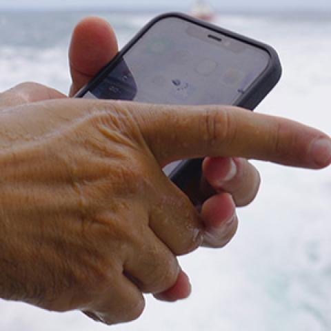 Closeup of hands of Hyannis Fire Chief holding a FirstNet-enabled cell-phone while on a boat at sea