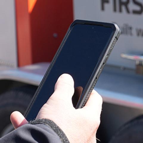 Police officer using a FirstNet enabled smartphone in front of a FirstNet SatCOLT