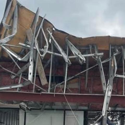 A person looks up at commercial building with the roof and storefront caved in from a tornado in Otsego County