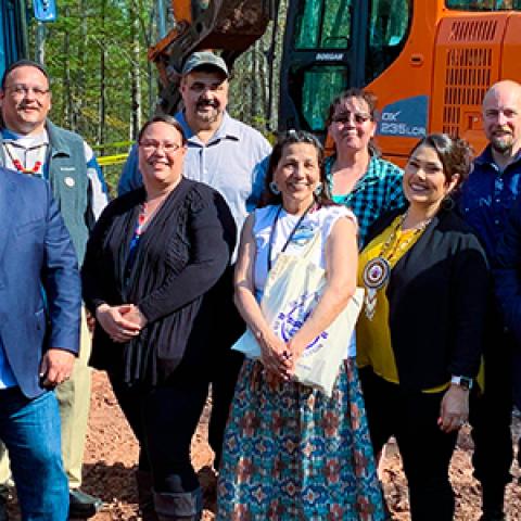 Eleven representatives who broke ground at a cell tower on the Red Cliff reservation stand in front of an excavator.