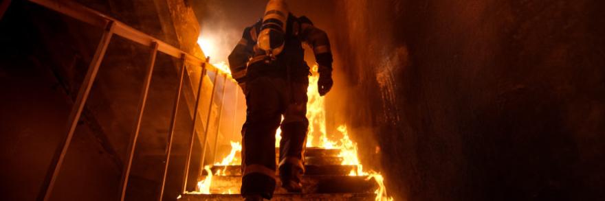 A firefighter ascends a flaming stairwell