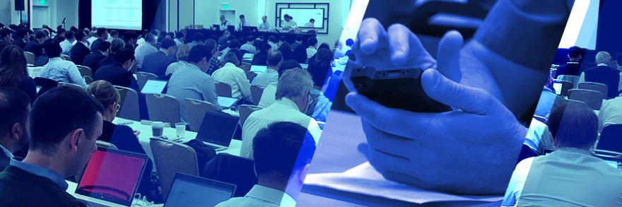 A room full of attendees at the June 2019 3GPP meetings listen and take notes on laptops as a panel of four speakers at the front give a presentation, a police officer holds a FirstNet enabled device