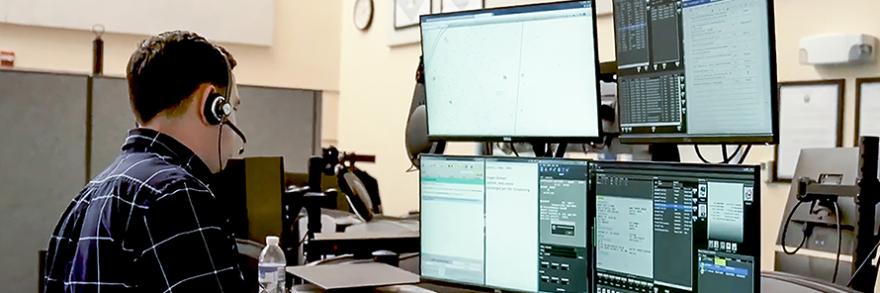 911 operator wearing a headset at a workstation with multiple screens