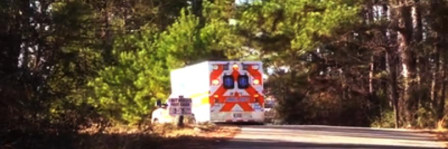 An ambulance drives down a small road on a sunny day. 