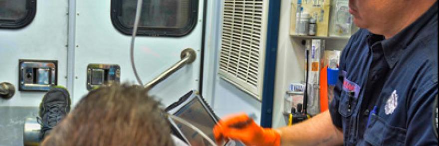 An EMS technician enters patient information into a laptop in the back of an ambulance