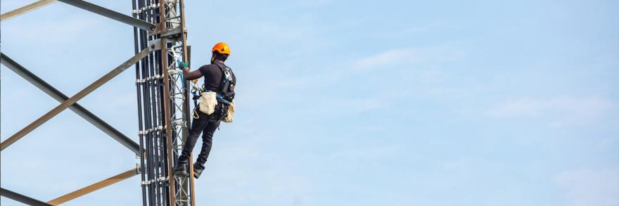 A worker wearing a harness and helmet climbs a cell tower