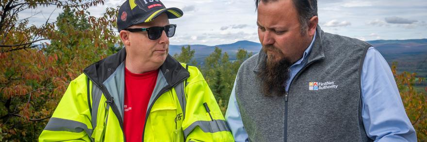 FirstNet Authority public safety advisor Bruce Fitzgerald talks with Jackman-Moose River Fire Chief Bill Jarvis with the mountains of Maine in the background during autumn
