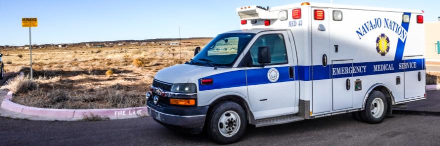 A Navajo Nation EMS ambulance parked on a street near an open field in New Mexico