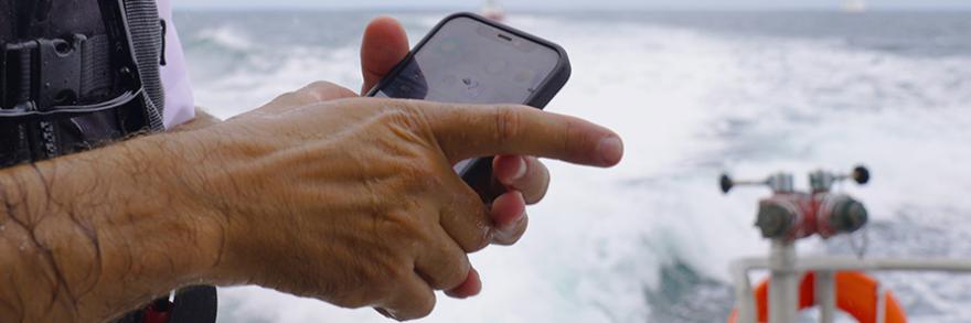 Closeup of hands of Hyannis Fire Chief holding a FirstNet-enabled cell-phone while on a boat at sea