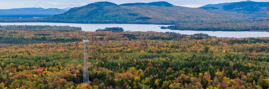In rural Maine, a broadband cell tower rises over a landscape of forests, mountains, and lakes. 
