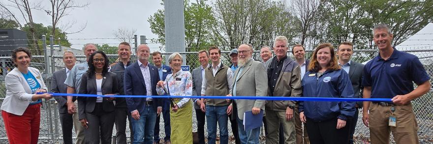 FirstNet Authority Executive Director and CEO Michael Cannon stands with federal, state and local leaders in front of a new cell tower with a blue ribbon in front. The mayor in the middle stands ready with scissors to cut the ribbon. 