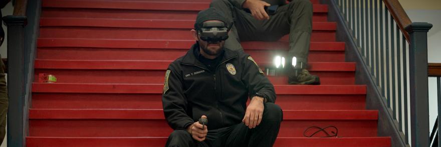 A police officer participating in the drone competition uses First-Person View (FPV) goggles and a remote control to maneuver a drone from a stairwell inside a Nashua middle school. 