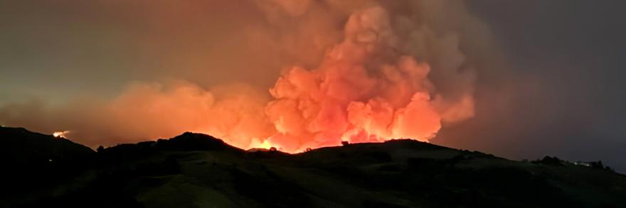The 2024 Airport Fire burns just beyond the ridge of Southern California’s Santa Ana Mountains while heavy smoke fills the sky. 