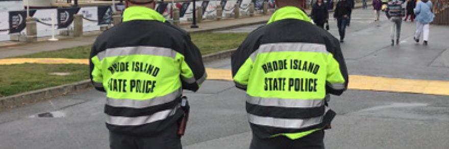 Two officers in Rhode Island State Police jackets look at the crowd at the 2018 Volvo Ocean Racenear the water