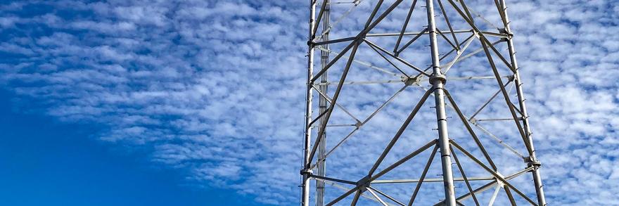 A broadband tower rises over a deep blue sky scattered with clouds