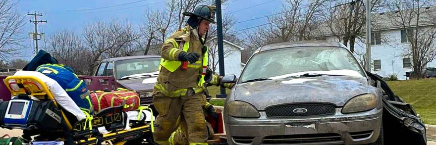 An EMS responder from the Bristol Kendall Fire Protection District with a stretcher at a damaged vehicle
