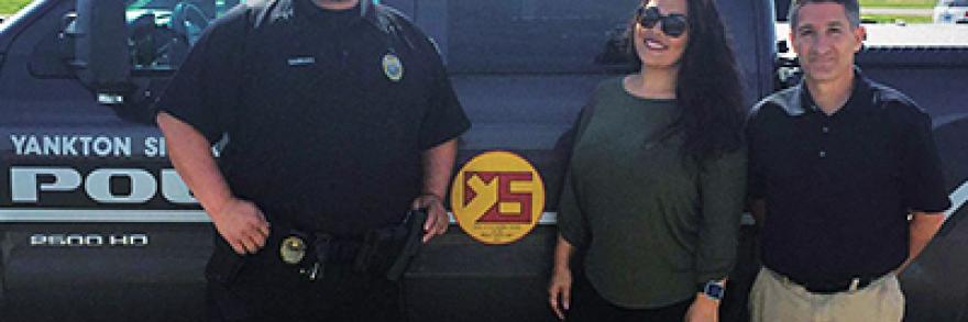 Two men and one woman stand in front of a Yankton Police truck. One of the men wears a police uniform.