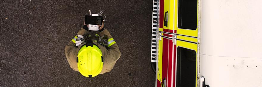 Aerial view of a firefighter wearing a helmet using a drone next to a firetruck 