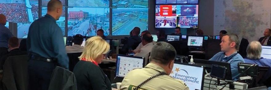 Emergency managers monitor computers during Kansas City Chiefs Super Bowl Parade; large screen projects live camera streams in emergency operations center in Kansas City, Missouri. 