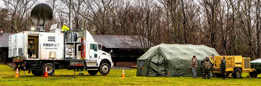 An AT&T SatColt and a tent are set up in a field near a forest. 
