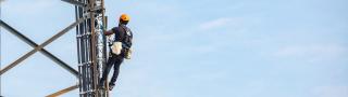 A worker wearing a harness and helmet climbs a cell tower