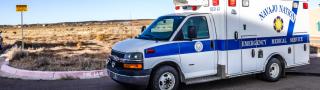 A Navajo Nation EMS ambulance parked on a street near an open field in New Mexico