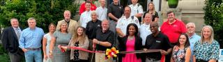 Group of officials and first responders standing in Allegany County, Maryland. Three people are holding a ceremonial ribbon, and one man cuts it with a large pair of scissors.