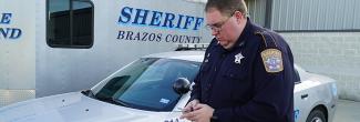 Deputy from Brazos Sheriff's Department looks at a smartphone standing in front of a mobile command vehicle