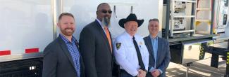 Sheriff Mike Hollinshead of Elmore County, Harry Markley from the FirstNet Authority and others stand in front of a FirstNet SatCOLT