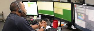 An emergency dispatcher sits in front of an emergency response system with his headset on.