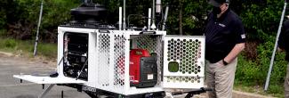 A man wearing a FirstNet shirt looks at a compact rapid deployable that is set up ready for use.