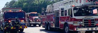 Three fire engines on the street with two fireman standing in front of one