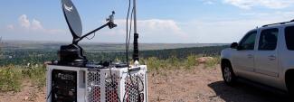 A FirstNet Compact Rapid Deployable on top of hill in Colorado in a rural area, the SUV that carried the CRD to the location is nearby