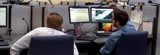 Two public safety officials look at multiple computer monitors at a workstation