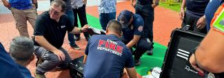 Members of the FirstNet Authority team and the Commonwealth of the Northern Mariana Islands Fire Department kneeling on the ground to demonstrate FirstNet assets during a multi-jurisdictional incident response communications exercise.