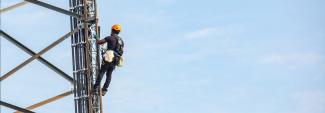 A worker wearing a harness and helmet climbs a cell tower