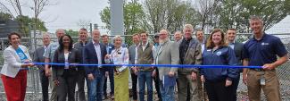FirstNet Authority Executive Director and CEO Michael Cannon stands with federal, state and local leaders in front of a new cell tower with a blue ribbon in front. The mayor in the middle stands ready with scissors to cut the ribbon. 